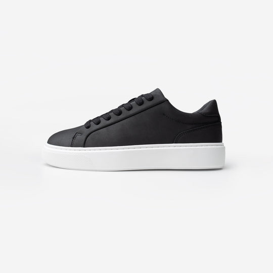 Side view of the Premium Classic Trainer in black, featuring a clean white PU upper, grey faux suede heel, white lace-up fastening and cushioned cup sole.