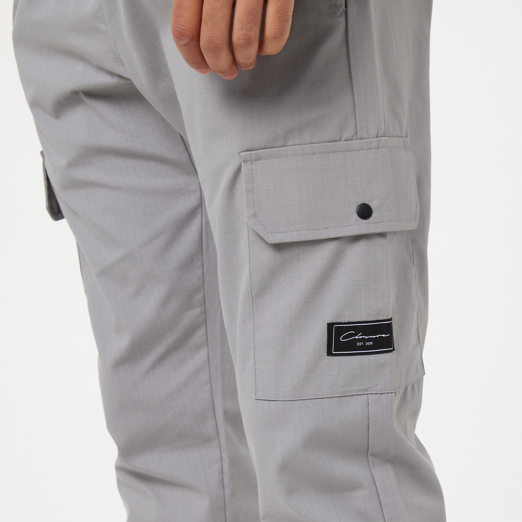 Ice grey men's cargo pants close up of pocket showing black patch logo of "Closure London"