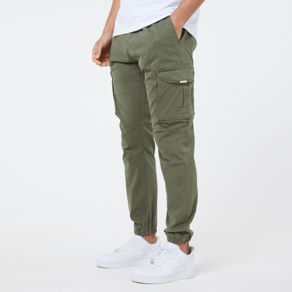 Male model wearing khaki men's cargo pants that are cuffed at the ankle styled with men's casual white trainers