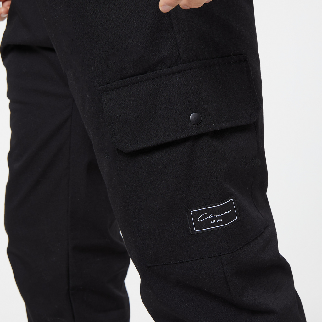 Close up of men's utility cargo trousers pocket with square "closure london" label logo 