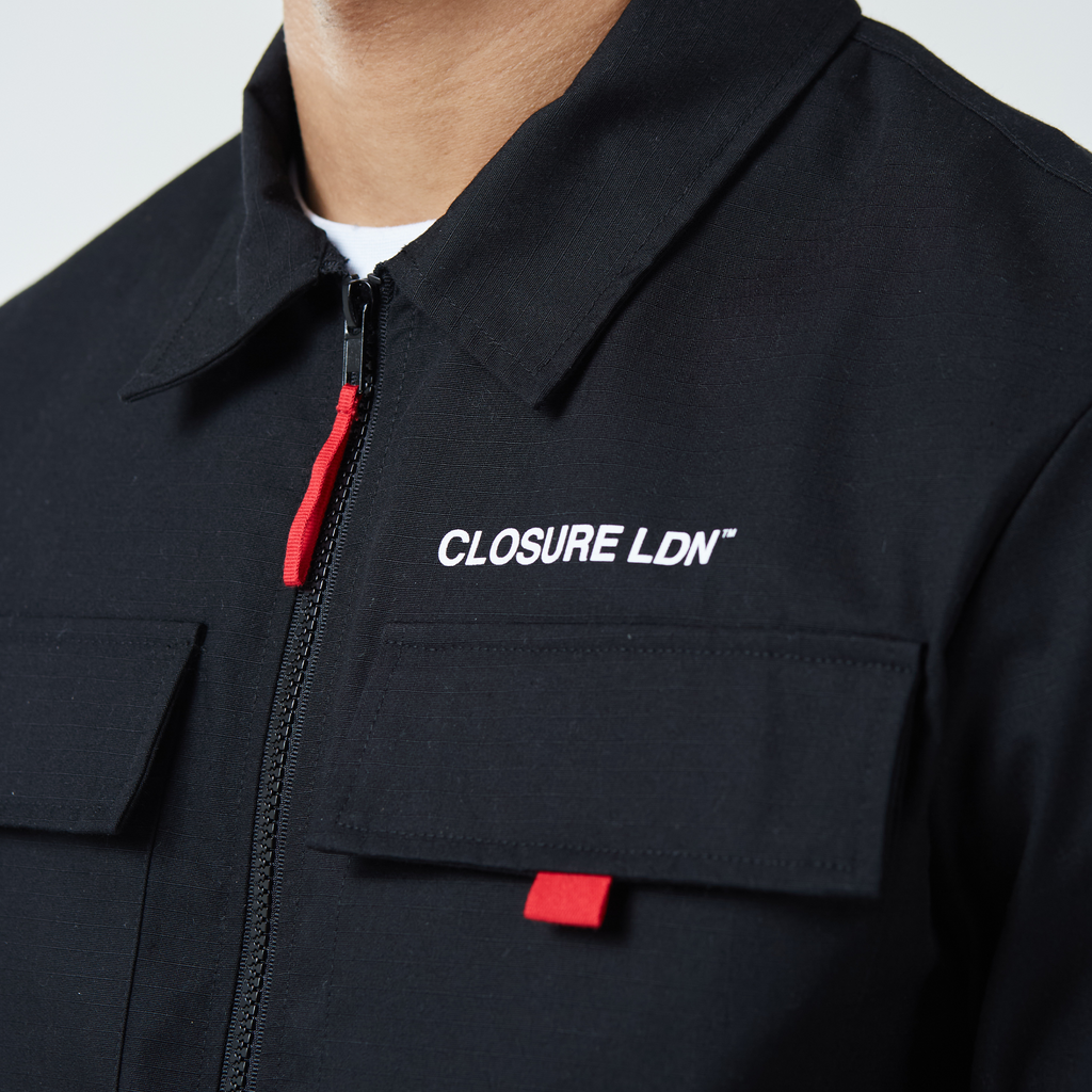 Close up of tech graphic black cargo overshirt jacket showing white "CLOSURE LDN" logo