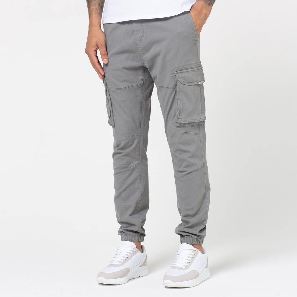 Man wearing cuffed grey cargo pants with his hand in the pocket and white trainers