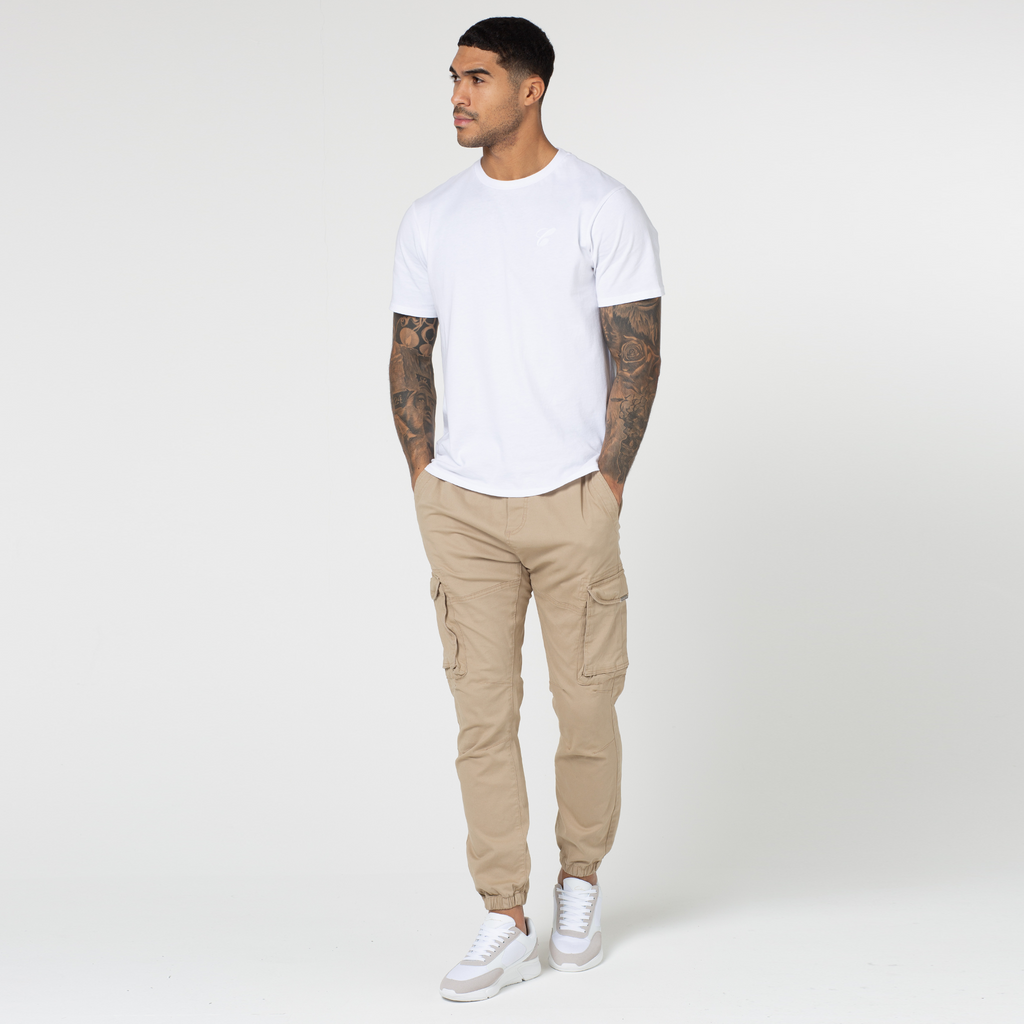 Male model styled in stone utility trousers that are cuffed with a white top and trainers 