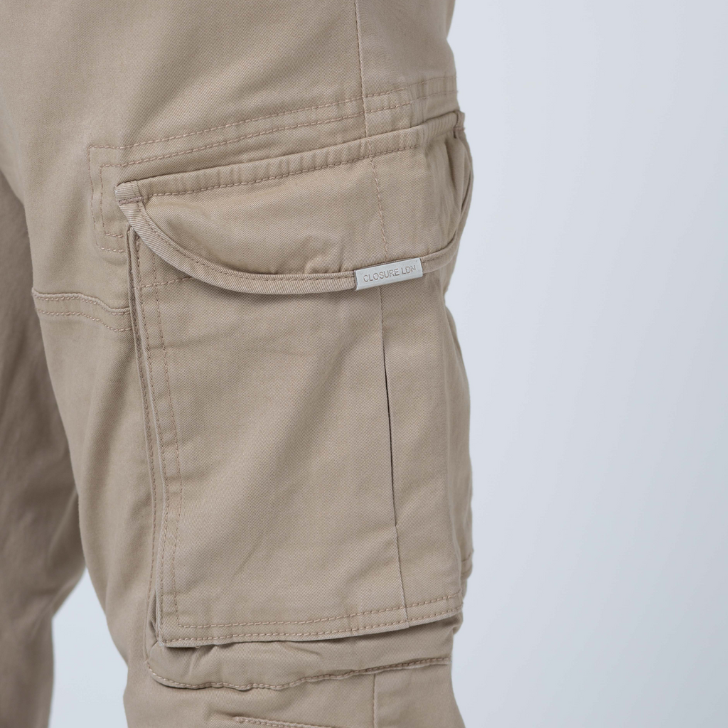 Pocket on beige utility trousers showing metal tag logo "CLOSURE LDN" printed on it