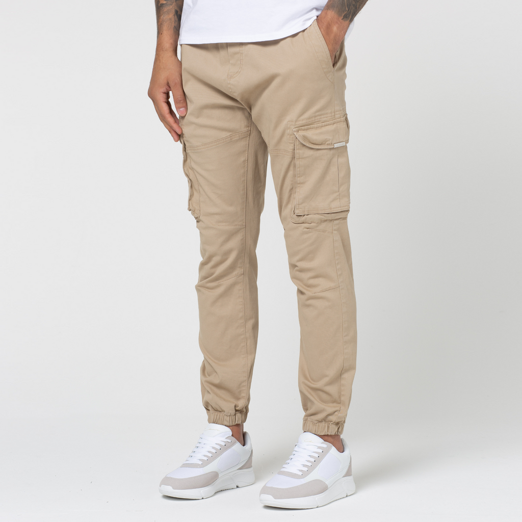 Model wearing cuffed men's cargo trousers in the colour stone paired with white and beige trainers
