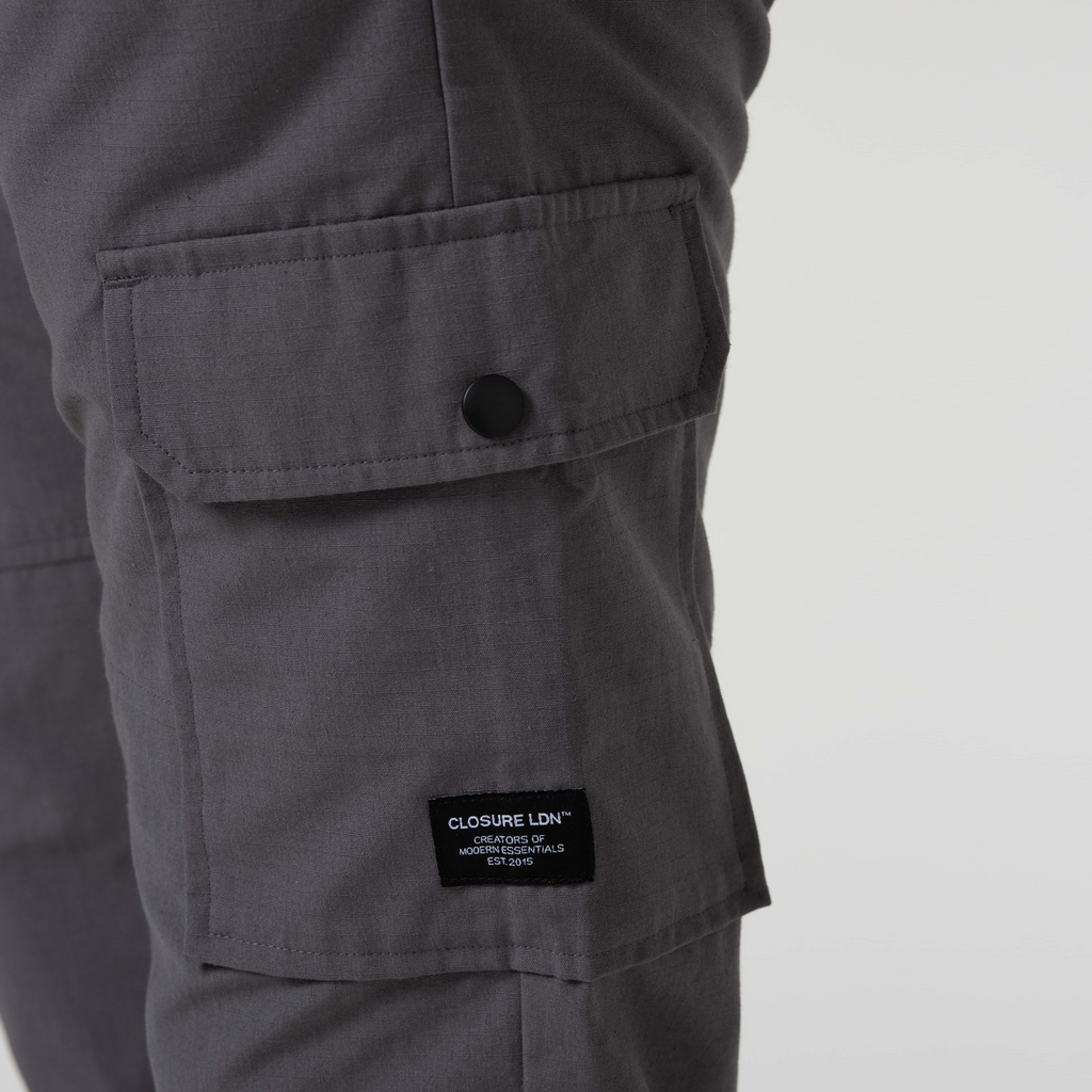 Close up picture of mens cargo trousers pocket with black button and black patch logo