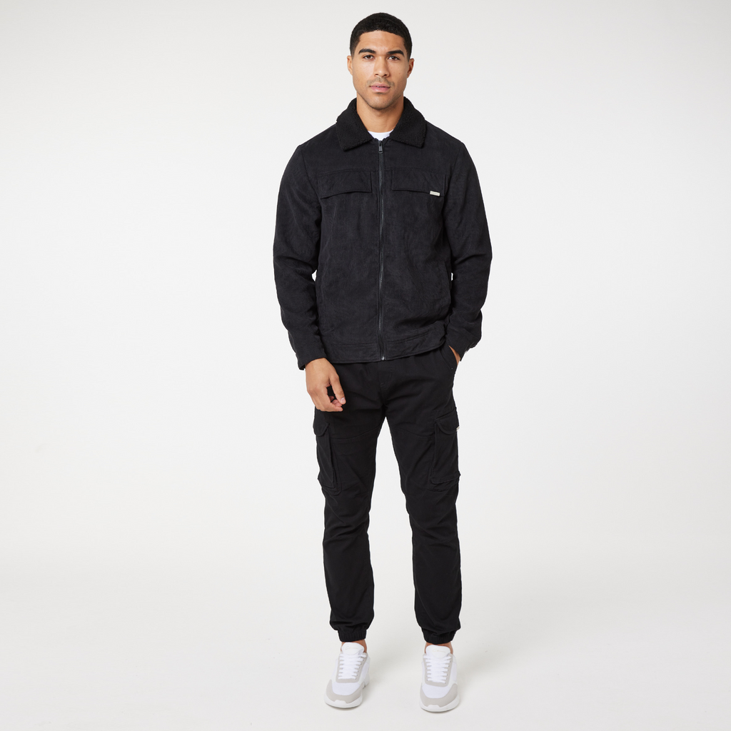Black corduroy overshirt jacket zipped up with matching trousers and white trainers