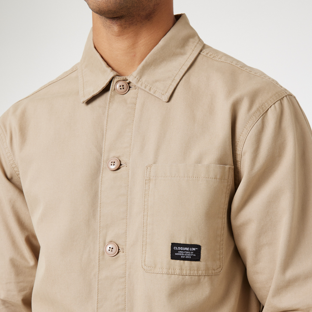 Close up of chore overshirt jacket pocket in stone with black "CLOSURE LDN" patch logo