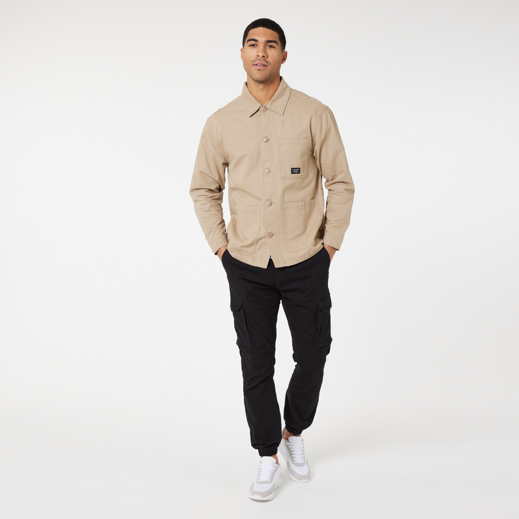 men's buttoned up overshirt jacket in beige styled with black pants and white trainers