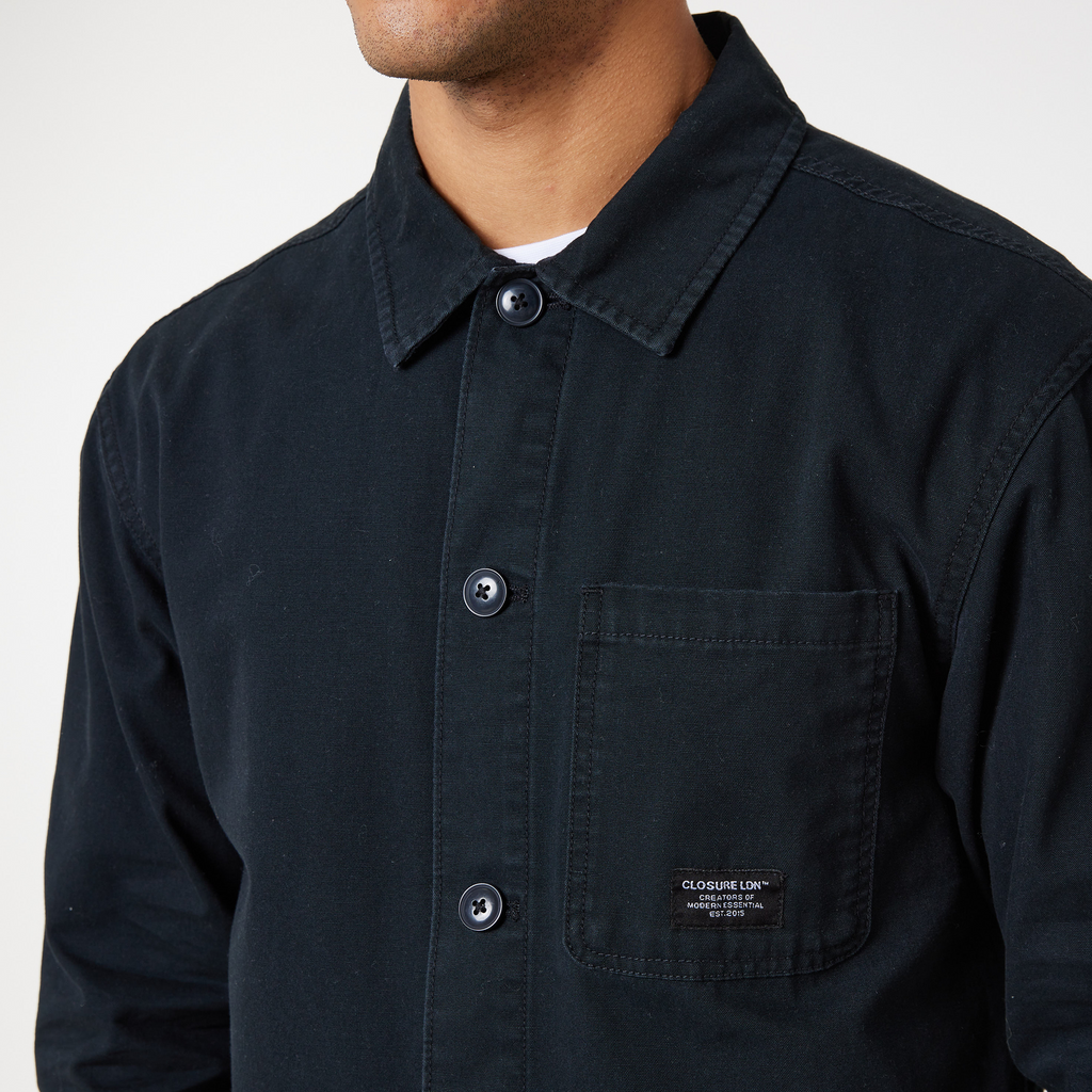 close up of buttoned up black overshirt jacket with a black "CLOSURE LDN" logo
