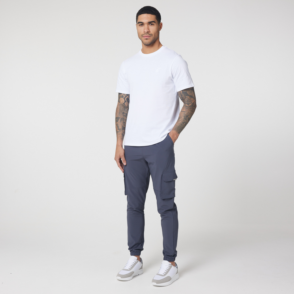 Model wearing dark grey utility trousers with plain white top and casual trainers