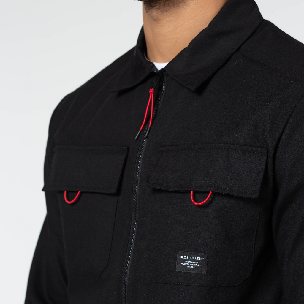 close up of black cargo overshirt with red detailing and "CLOSURE LDN" logo 