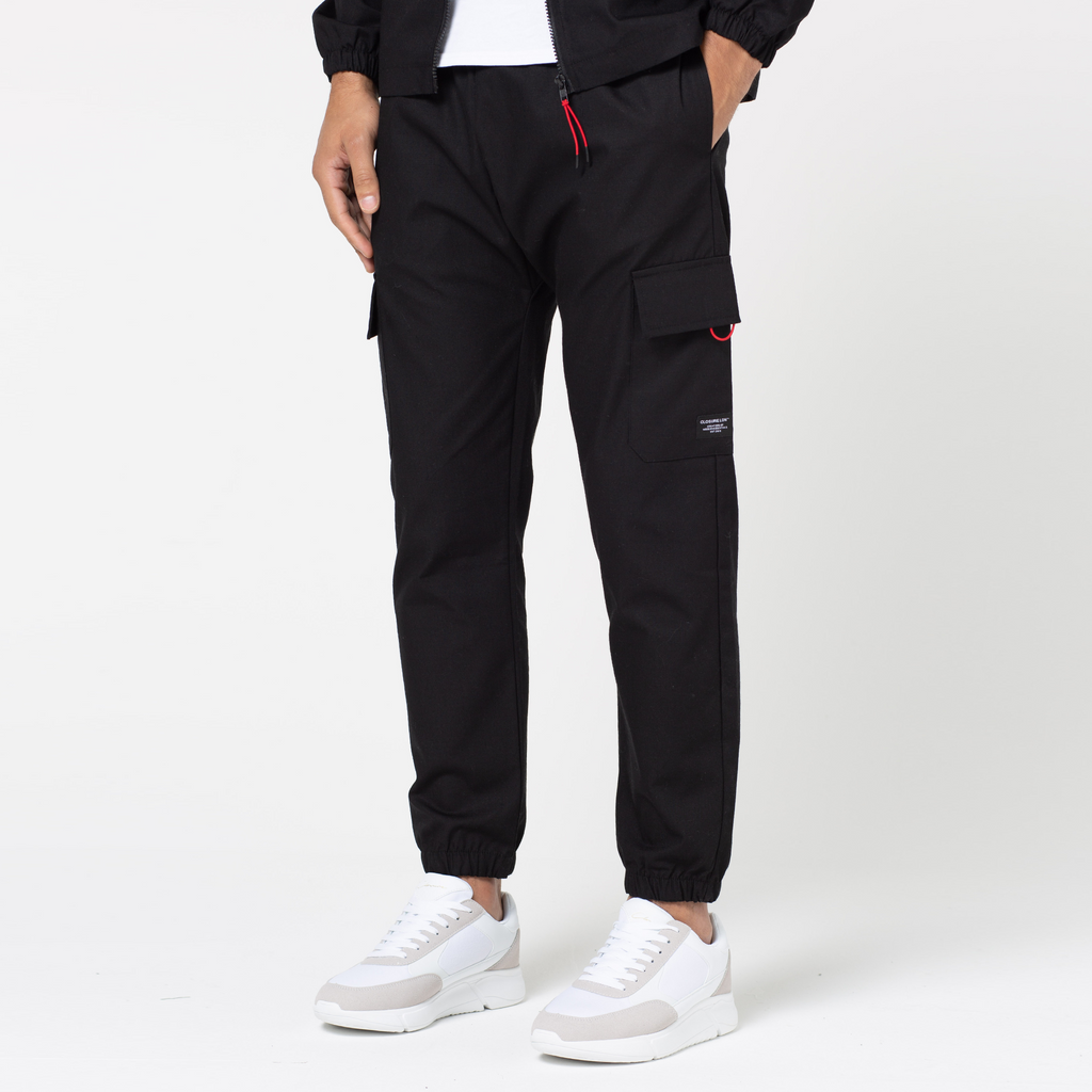 Men's tech utility trousers in black and red that are cuffed at the ankle paired with white trainers