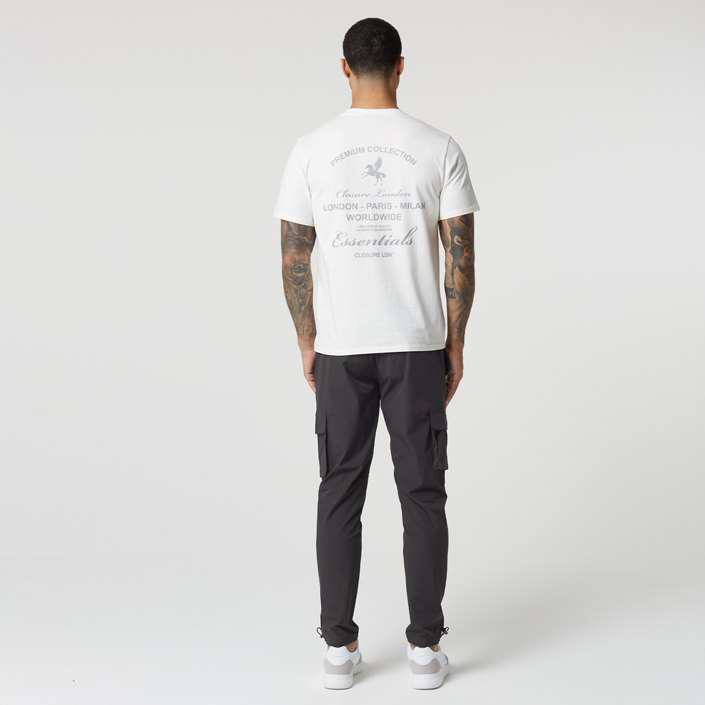Back profile of model wearing dark grey utility trousers with a white tee that has grey logo