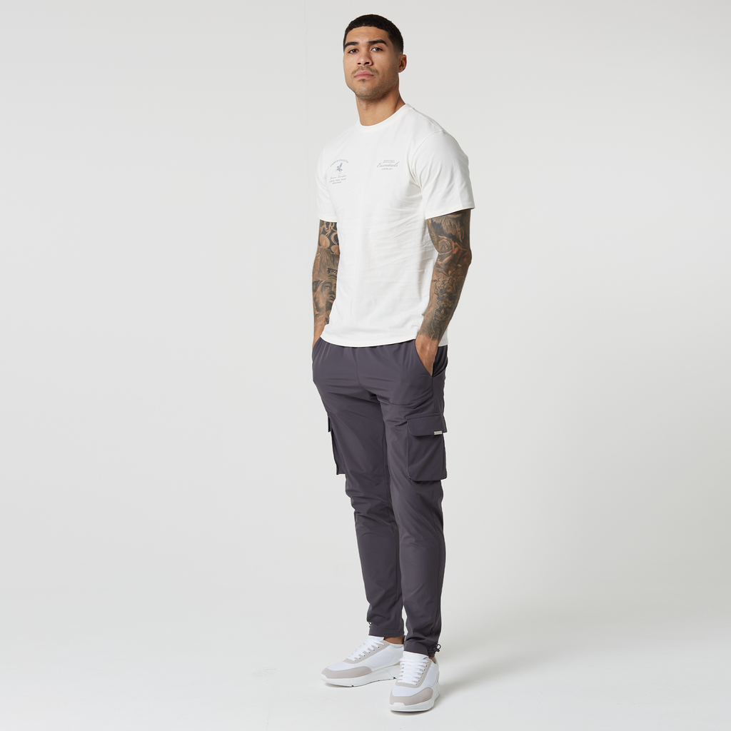Model wearing utility trousers in dark grey with white and grey logo top and trainers