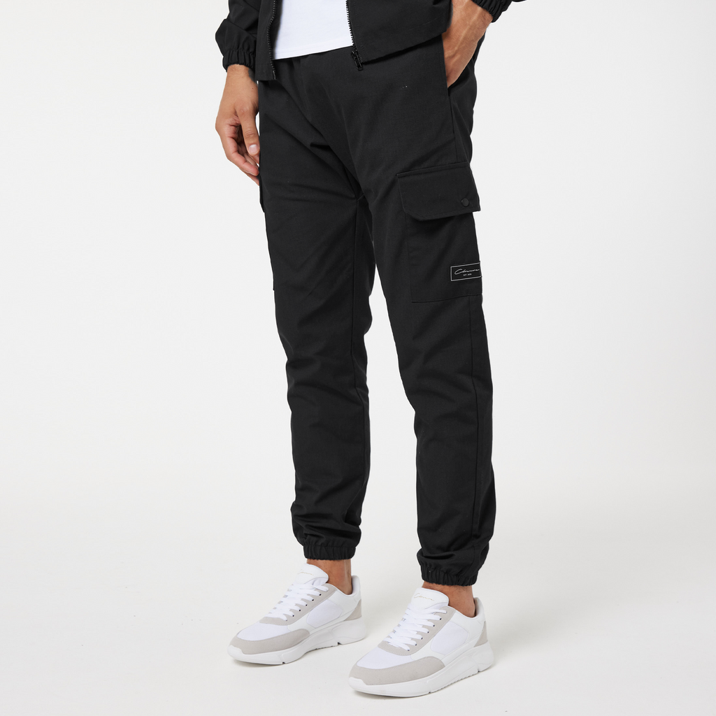 Model wearing mens cargo pants in the colour black cuffed at the bottom with white casual trainers