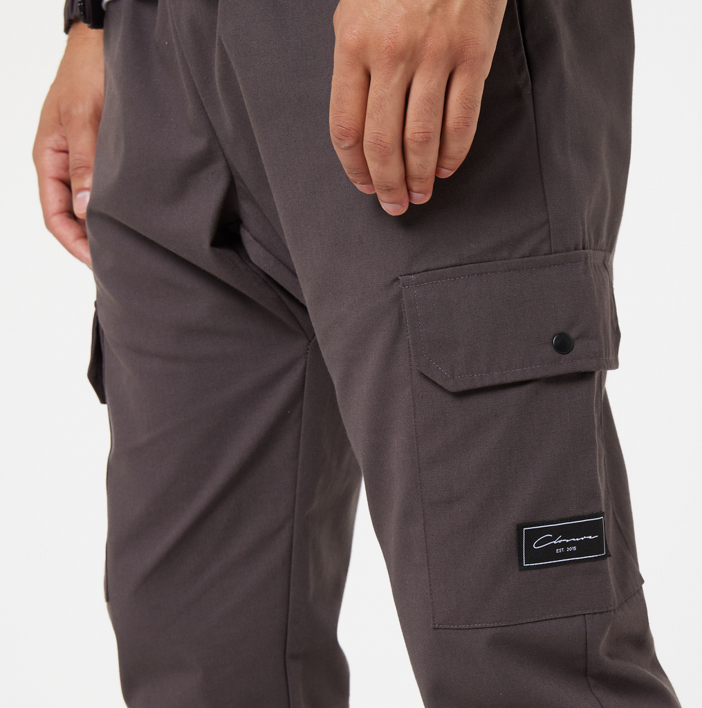 close up of mens cargo pants pockets with black popper button and black "Closure London" logo
