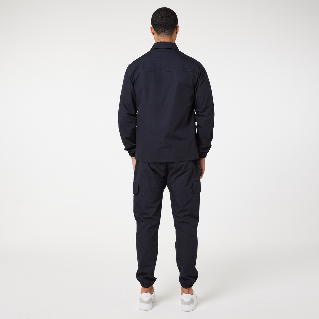 Back profile view of utility cargo pants in navy with matching navy overshirt and white trainers