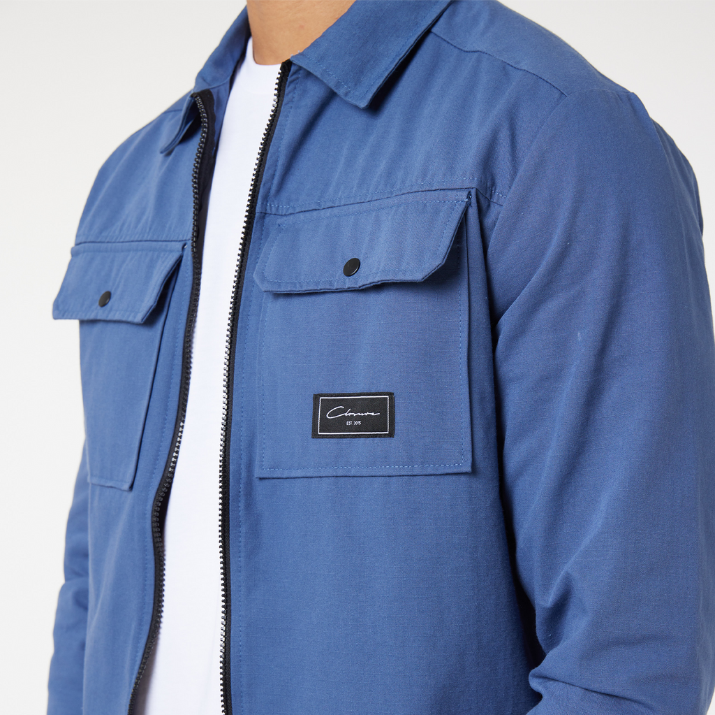 close up of men's zip overshirt pockets in blue with black "closure london" patch logo