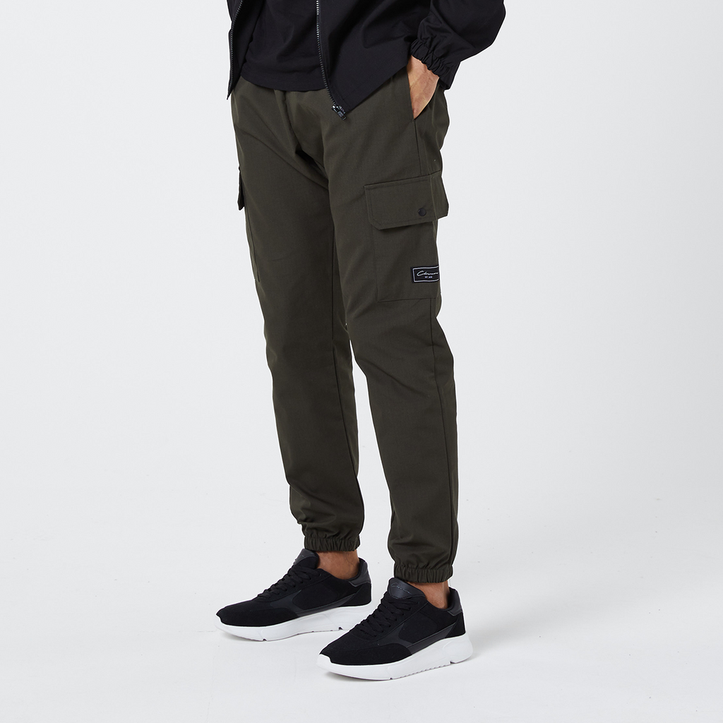 Men's khaki utility cargo pants that are cuffed at the ankle paired with black and white trainers